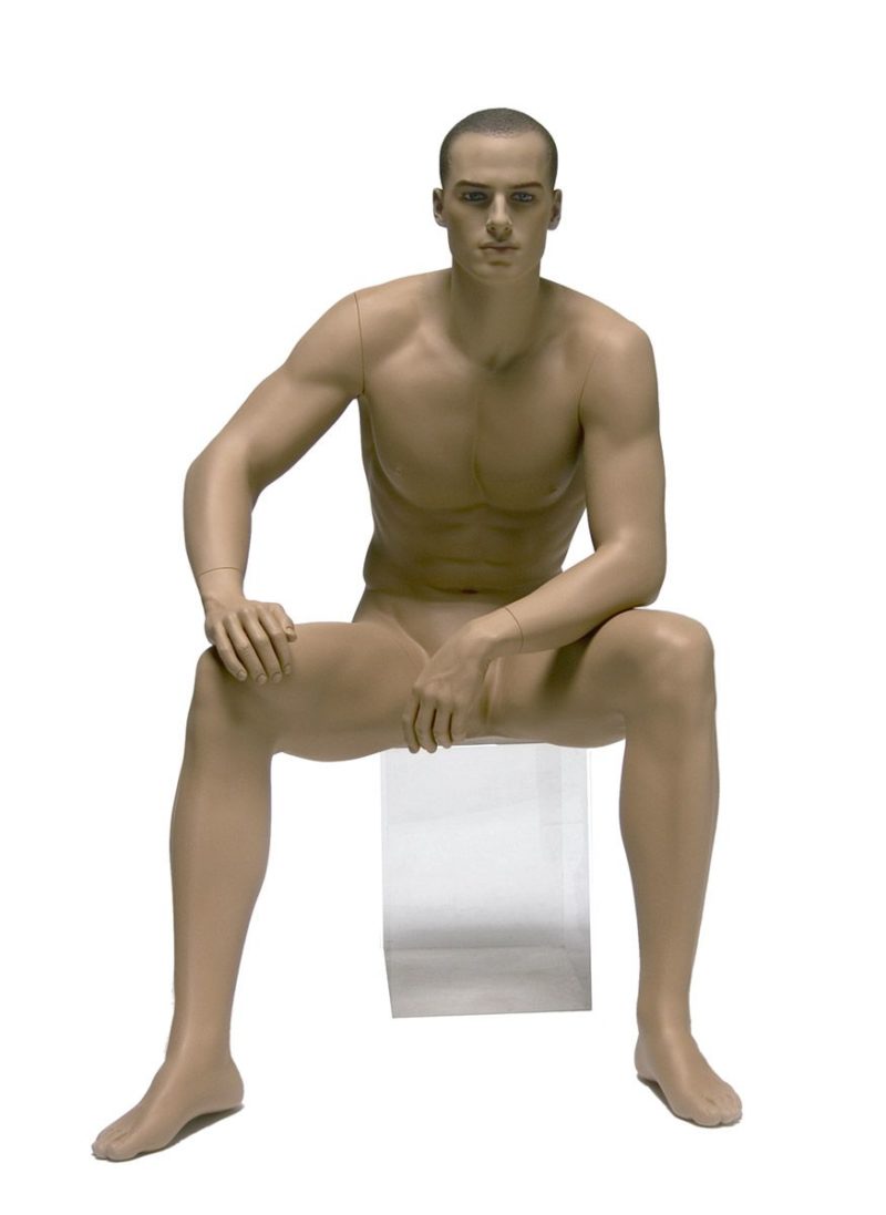 Maniquí de hombre maquillado, con la cara esculpida, sentado y ligeramente inclinado hacia el frente, con un brazo apoyado sobre las piernas, color carne
